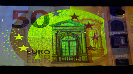 checking money held in a human hand . Euro currency in UV light protection