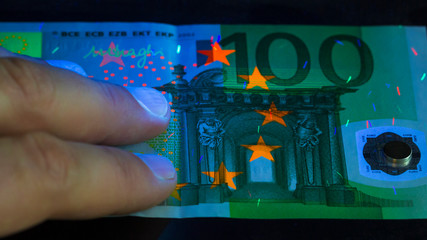 checking money held in a human hand . Euro currency in UV light protection