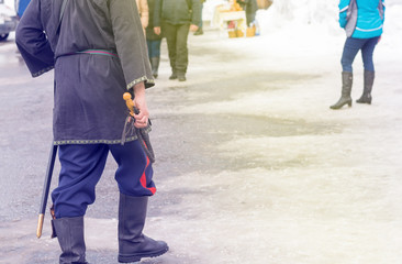 Cossack whip in the hand of a Cossack who goes in national costume, in kirzov boots and with a saber in winter on a crowded street - obrazy, fototapety, plakaty