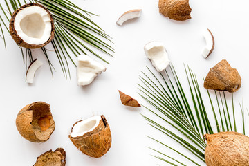Fototapeta na wymiar Coconuts pieces background with palm leaves on white table top-down