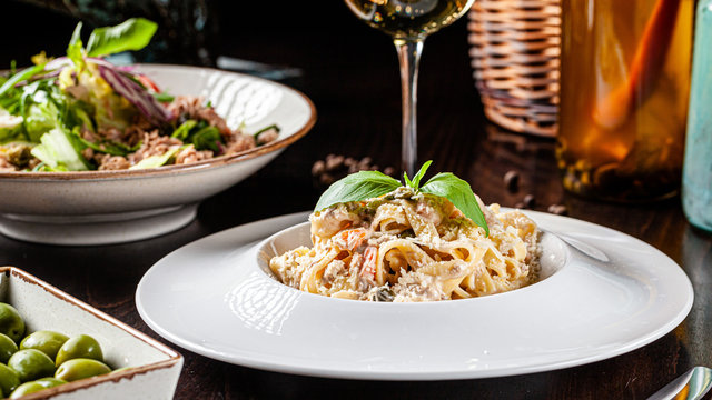 Spanish cuisine. Pasta in cheese sauce with canned tuna fish, cherry tomatoes and parmesan and basil. Dishes in a restaurant in a white plate. background image, copy space text