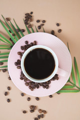 A Cup of black hot coffee on a trendy pastel background with a palm branch and coffee beans . Top view