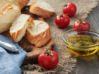 Fresh sliced baguette, tomatoes and olive oil, ingredients for making a sandwich, closeup. Rough fabric background