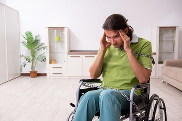 Young male invalid in wheel-chair suffering at home