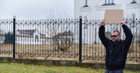 Street photo of an adult Caucasian man with a banner in his hands in a black jacket in the afternoon
