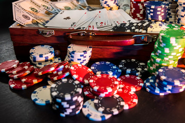 Colorful poker chips with playing cards and american dollars on dark background.