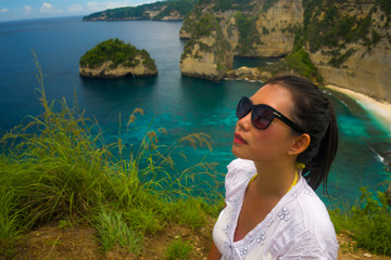 Fototapeta na wymiar happy Asian Korean woman in sunglasses enjoying amazing coast scene from view point at tropical paradise beach with diamond rock cliff cheerful during summer holidays