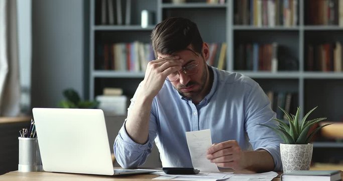 Stressed businessman accountant feeling worried about bankruptcy calculating financial data. Overwhelmed man checking bill having financial money problem bank debt concept sitting at home office desk.