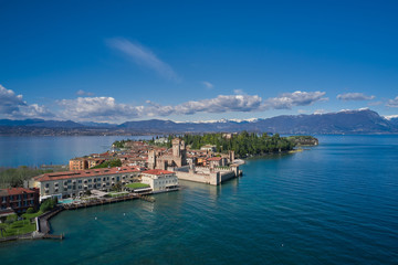 Sirmione town, Lake Garda, Italy. Aerial view of Sirmione. The historical part of the city.  In the background mountains in the snow and blue sky.  Side view of the island.