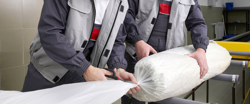 Men Workers Packing Carpet In A Plastic Bag After Cleaning It In Automatic Washing Machine And Dryer In The Laundry Service