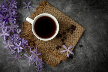 Purple flower and black coffee cup on cement background.