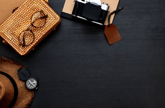 summer travel flat lay of traveller accessories set.hat,yellow wicker bag,camera and notebook on black wooden table with copy space