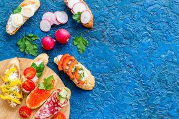 Set of bruschetta on cutting board on blue background top-down copy space