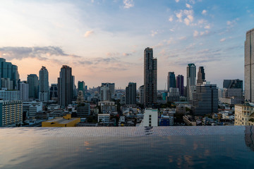 Aerial cityscape of picturesque Bangkok at sunset from rooftop swimming pool view. Panoramic sunrise skyline of the biggest city in Thailand. The concept of metropolis.