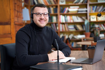 Male blogger streaming from library using laptop and microphone