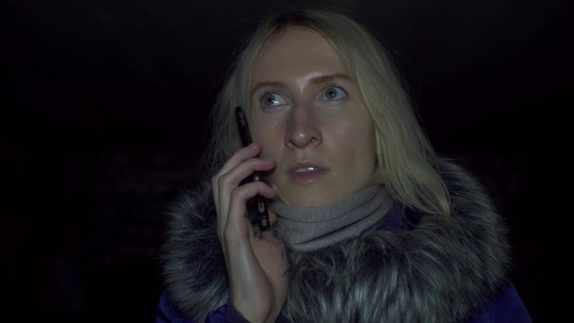 Portrait of shocked scared young woman. She is lit by police flashing lights and is talking on phone. woman is scared, desperately wants something, covering her mouth with hands of problem.