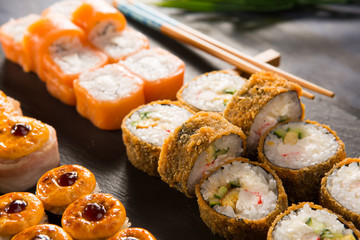 Set of baked sushi rolls with wasabi and ginger on a black background. Japanese oriental cuisine
