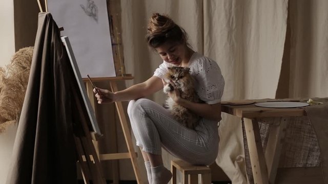 Girl with a cat in an art studio. Easel and light from the window.