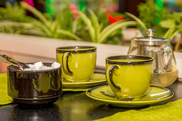 Two green mugs of tea and a sugar bowl are on the table