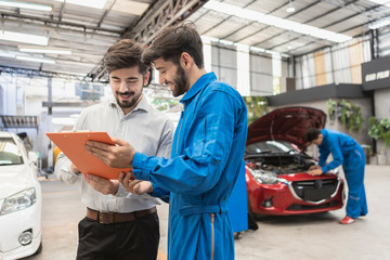 A mechanic and customer look at paper. service car in garage is paper checklist car. service car, repair, maintenance concept.Technician doing the checklist for repair machine a car in the garage.
