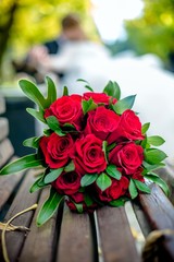 A wedding bouquet of red roses lies on a bench