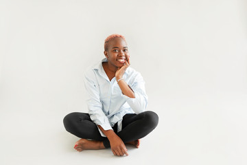 Beautiful african teenage girl with pink hair sitting in studio on white background - Powered by Adobe