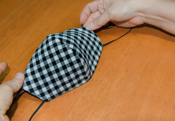 Woman making a homemade mask from black and white plaid and nano fabric, Housewife made cloth face protective mask handmade from tartan cloth,Mask for protection nose and mouth on wood table backgroud