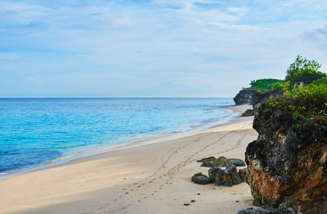 Scenic sea landscape. High cliff on tropical beach in Bali, Indonesia. Tropical nature. Beautiful turquoise sea water, white sand beach and green tropics of Bali shoreline.