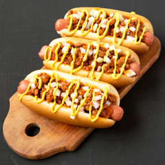 Homemade Detroit style chili dog on a rustic wooden board on a black background, low angle view. Close-up.