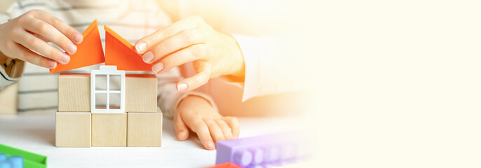 Mom and child build a house of wooden cubes and blocks constructor. Close up of hands holding roof elements. Playing parents and children at home. Credit, real estate and mortgage financial concept.