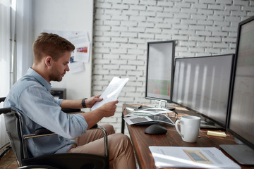 Analyzing data. Side view of young male businessman in a wheelchair looking at financial reports...