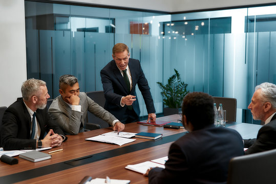 It is your fault. Angry mature businessman in formal wear shouting at his colleagues and pointing finger while having a meeting in the conference room