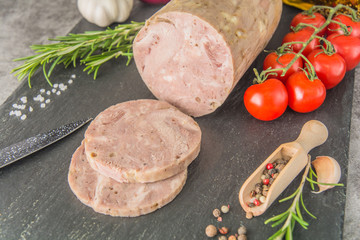 Closeup Homemade ham sausage, sliced on black slate, with spices, appetizers and a knife.