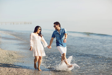 Happy couple walking and playing on the beach, soaking his feet in the water. Wonderful love story in Rimini, Italy