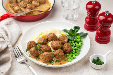 meatballs with mashed potato, cream sauce and green peas on white plate