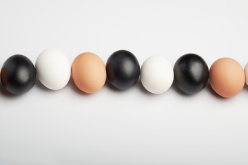 Row of eggs of different colors on a white background. Black, white and brown chicken eggs.
