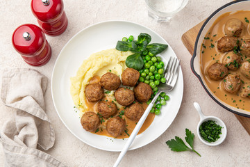 meatballs with mashed potato, cream sauce and green peas on white plate, top view