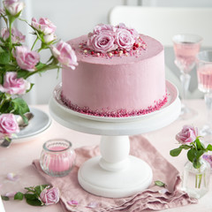 festive pink cake on white cake stand decorated with fresh rose