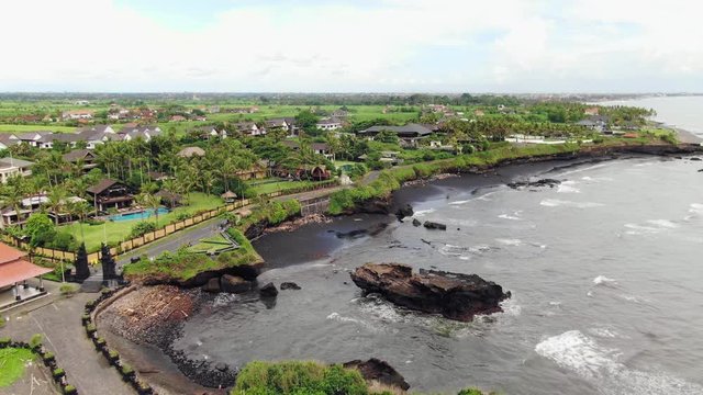 Aerial Pura Gede Luhur Batu Ngaus, Bali, Indonesia. Drone Fly-by of coast and town. Cloudy day.
