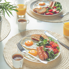 breakfast with fried eggs, sausages, fresh vegetables, coffee and orange juice on white table