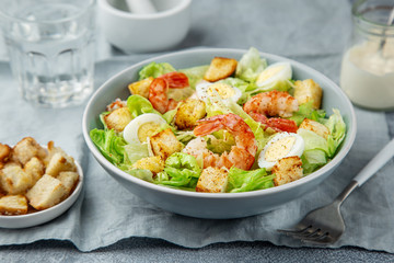 Caesar salad with prawn, roasted chicken,  croutons and cheese in blue bowl
