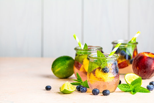 Blueberry and peach infused water, cocktail, lemonade or tea in jar with water drops. Summer iced cold drink with blueberry, lime, peach and mint