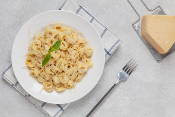 Italian pasta tortellini with Parmesan and basil on a plate. Traditional Italian pasta. Top view. 