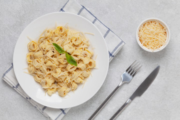 Italian pasta tortellini with Parmesan and basil on a plate. Traditional Italian pasta. Top view. 