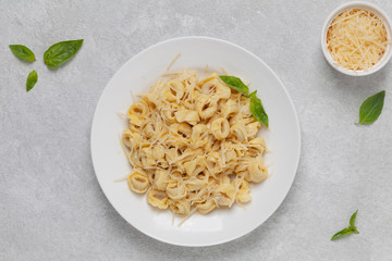 Italian pasta tortellini with Parmesan and basil on a plate. Traditional Italian pasta. Top view. 