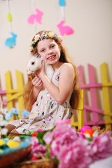 Obraz na płótnie Canvas child-a little girl in a dress and a flower wreath on her head smiling and holding an Easter Bunny on the background of flowers and decor