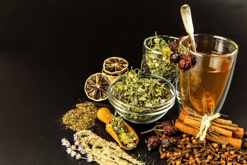 Cup of herbal tea. Various herbal tea ingredients in glass jars over black background. Traditional medicine against flu and cold.
