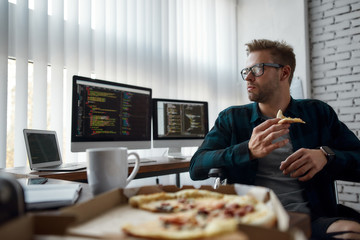 Taking a break. Portrait of hungry male web developer in a wheelchair eating pizza while sitting at...