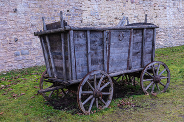 Fototapeta na wymiar The broken ancient medieval rural wood cart or wagon on the green grass on the background of the castle or fortress stone or brick wall 