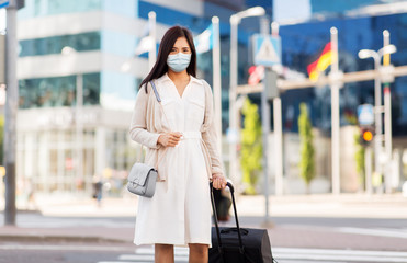 Fototapeta premium health, people and tourism concept - happy young asian woman wearing protective medical mask for protection from virus with travel bag on city street